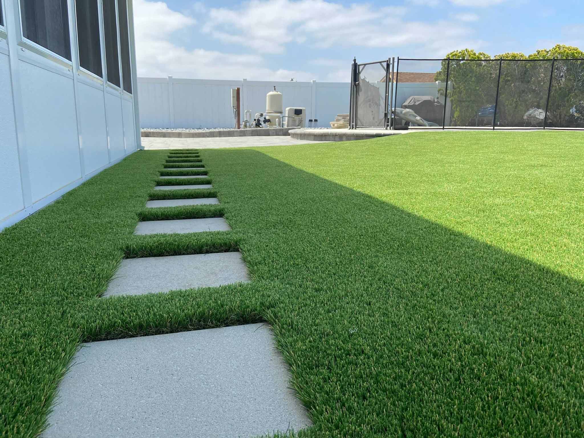 Front yard of a house with artificial grass and stepping stone pathway leading to the entrance.