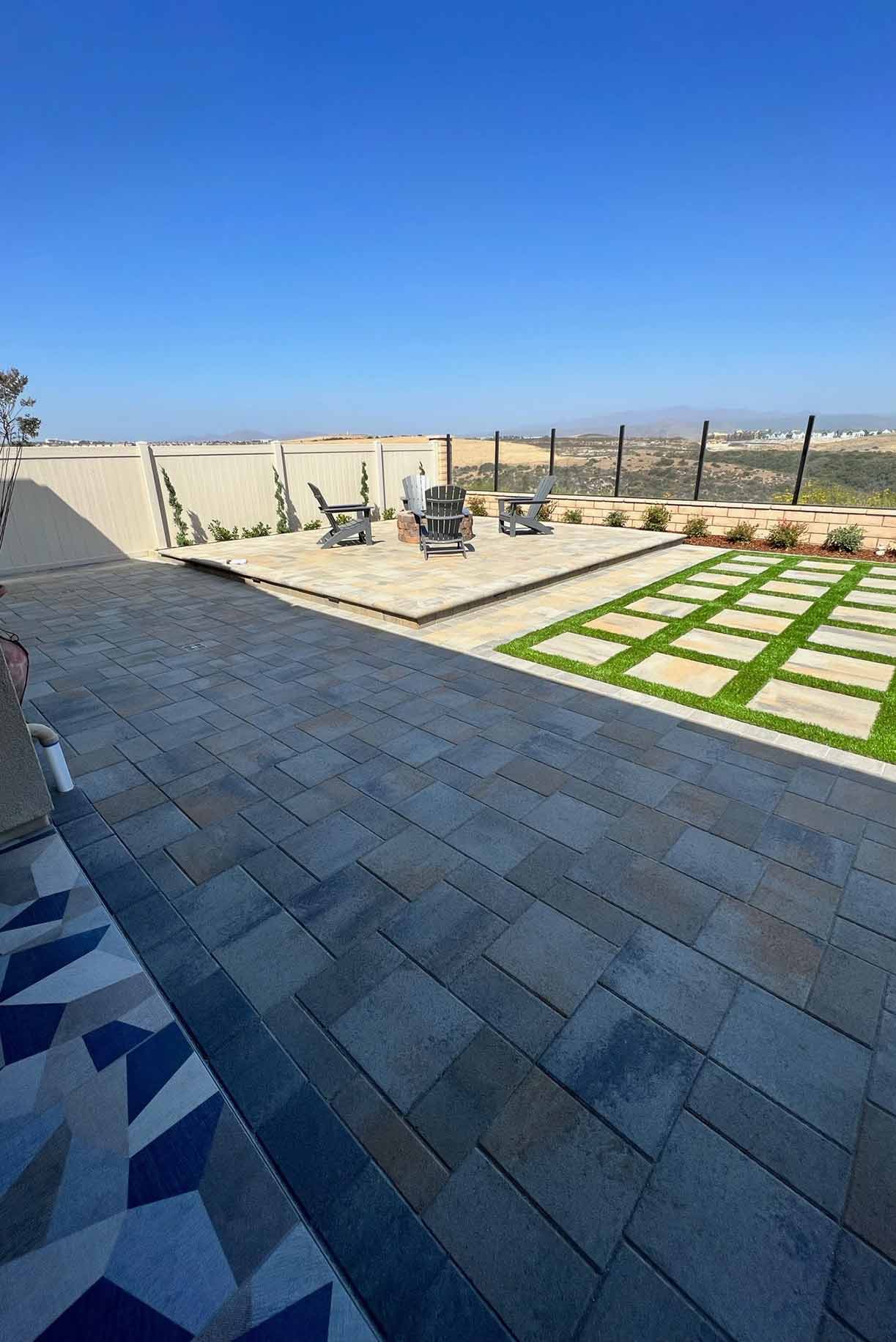 Backyard patio with a covered pergola, ceiling fans, a table holding boxes, artificial grass, and a two-story beige house.