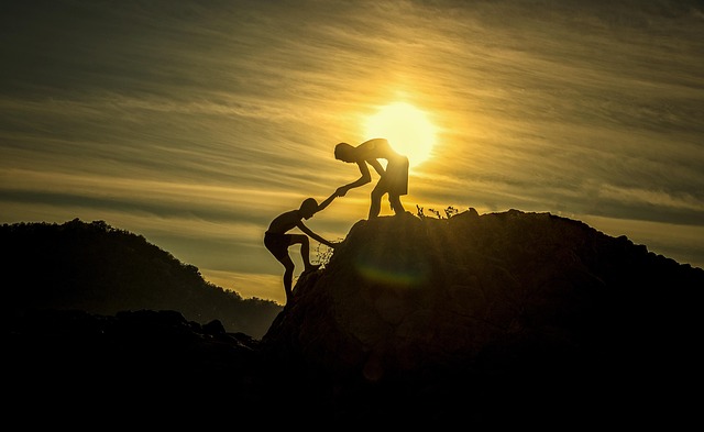People helping each other in the foreground of a beautiful sunset