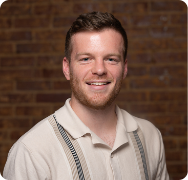 Smiling person in white shirt with suspenders against brick wall