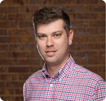 Professional headshot of a person in a checkered shirt against brick wall