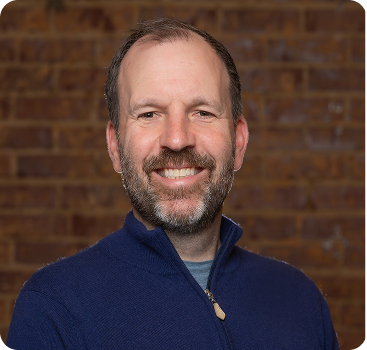 Smiling man in blue jacket standing in front of brick wall