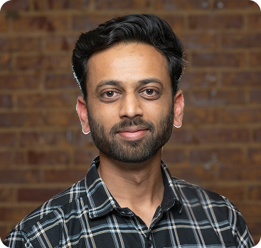 Professional portrait of a person in a plaid shirt against brick wall