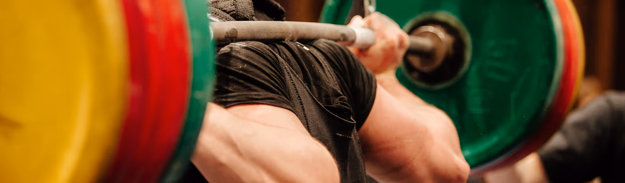 Close-up of a person lifting a barbell with colorful weight plates during a weightlifting exercise.