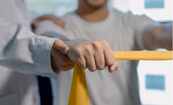 A therapist assisting a person with a yellow resistance band exercise for shoulder rehabilitation.