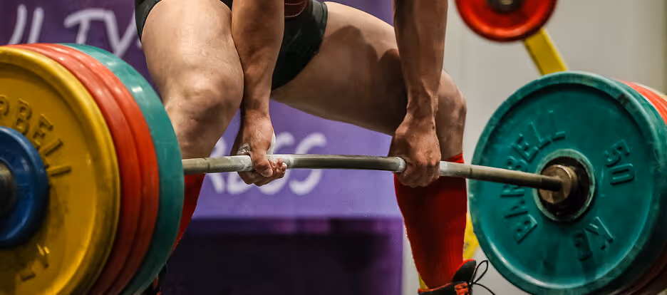 Close-up of a weightlifter gripping a barbell loaded with colorful heavy weight plates during a deadlift.