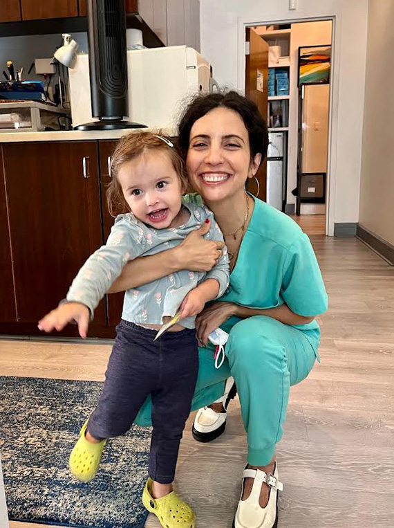 A woman in scrubs holding a child, both smiling and posing for the photo.