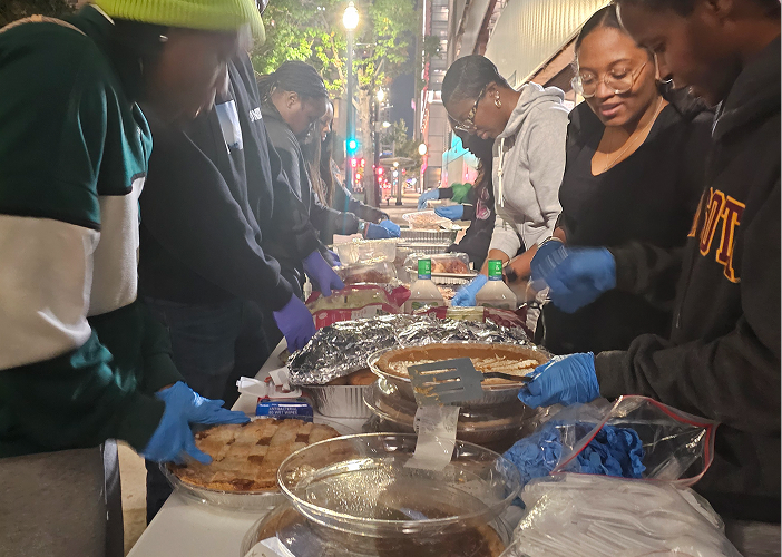 Volunteers wearing gloves serving food dishes on a table outdoors at night.