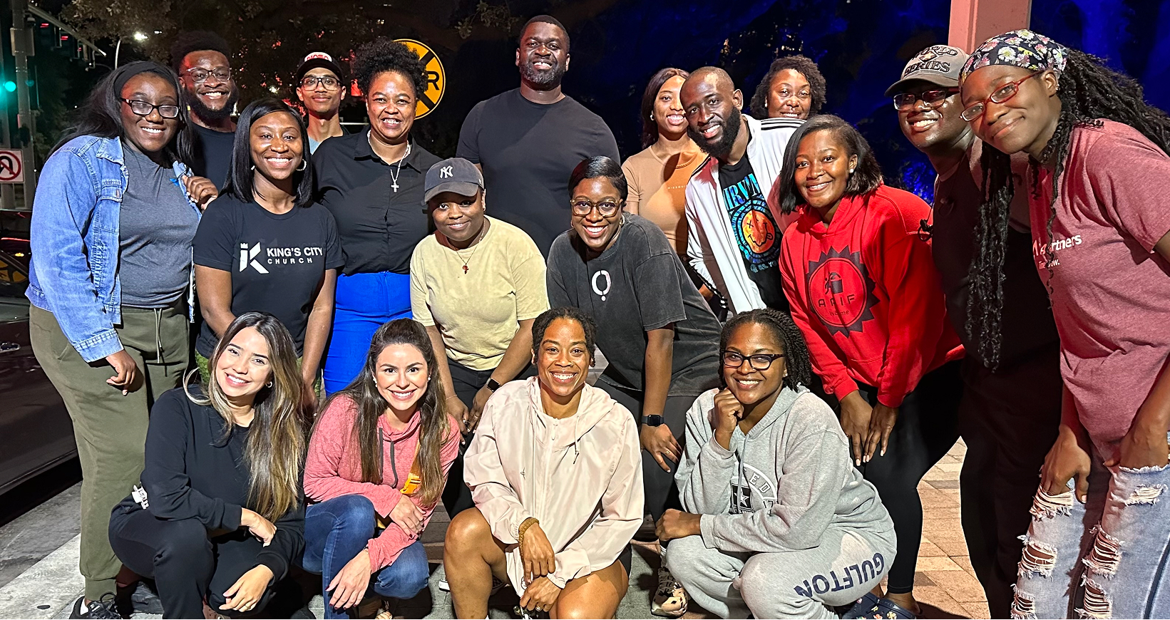 Group of diverse young adults smiling and posing together outdoors at night.