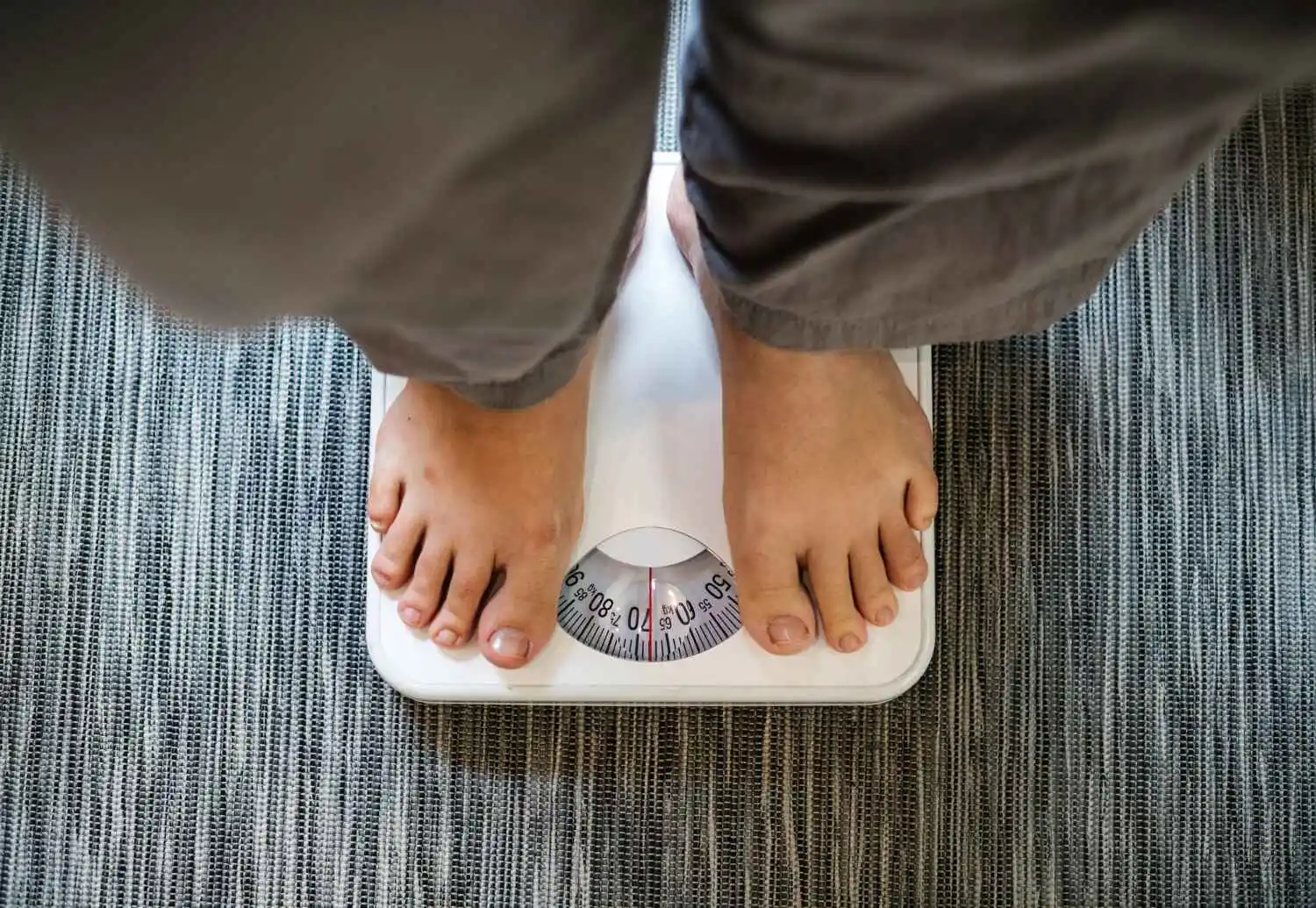 Man looking down at a scale, illustrating concerns about weight gain potentially associated with low testosterone levels.