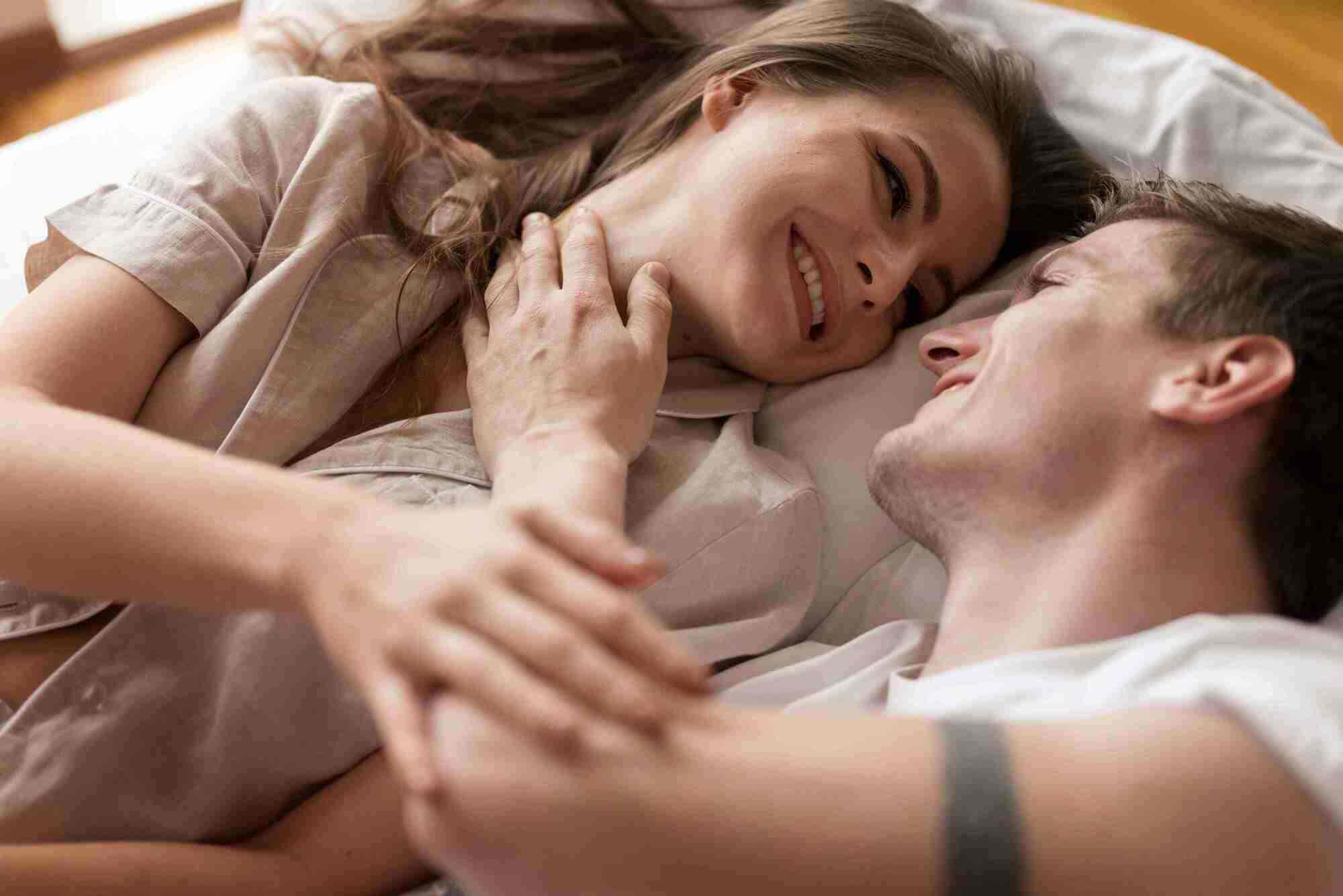 Smiling couple lying in bed together, symbolizing restored intimacy and improved confidence through Viagra treatments.