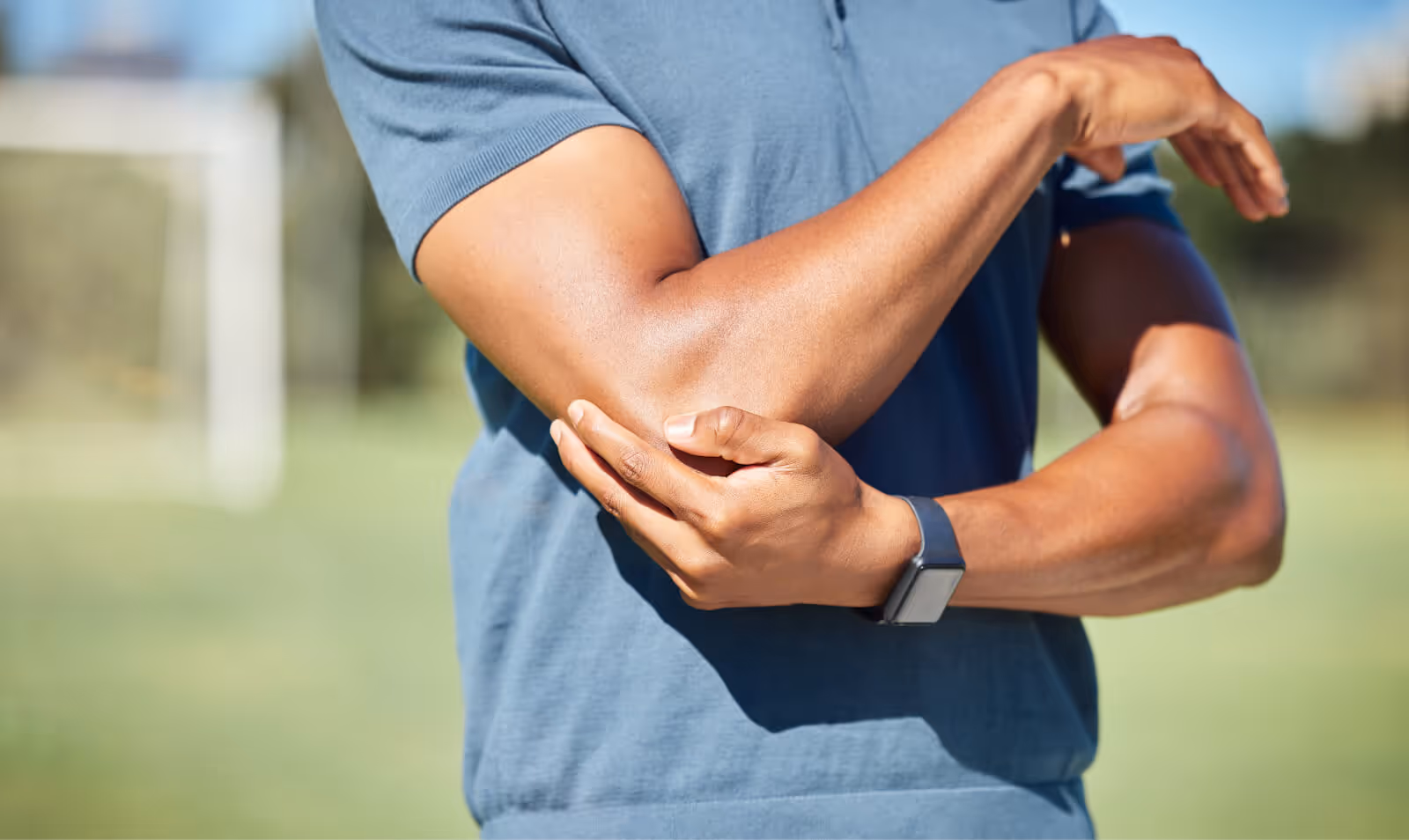Man holding elbow outdoors, representing joint pain potentially linked to low testosterone levels and treatment options at Gameday Men’s Health.