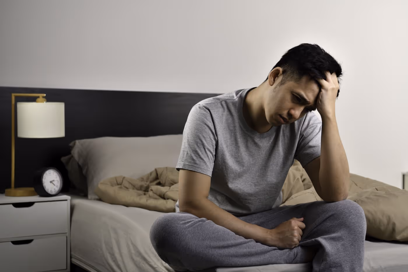 A man sits on a bed, hand on his head, reflecting on low testosterone and depression.