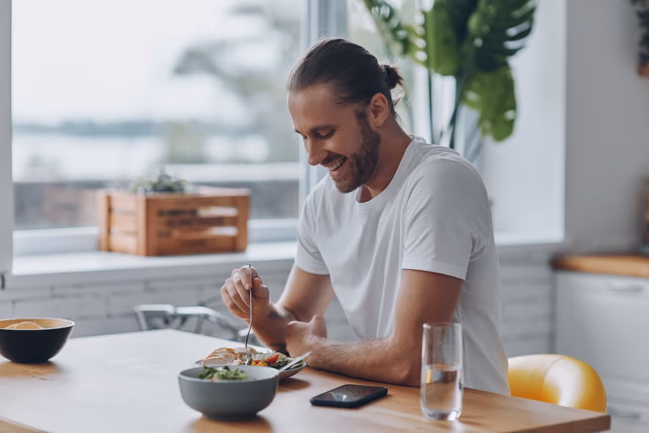 Smiling man enjoys a salad, reflecting a healthy lifestyle to manage estrogen on TRT.