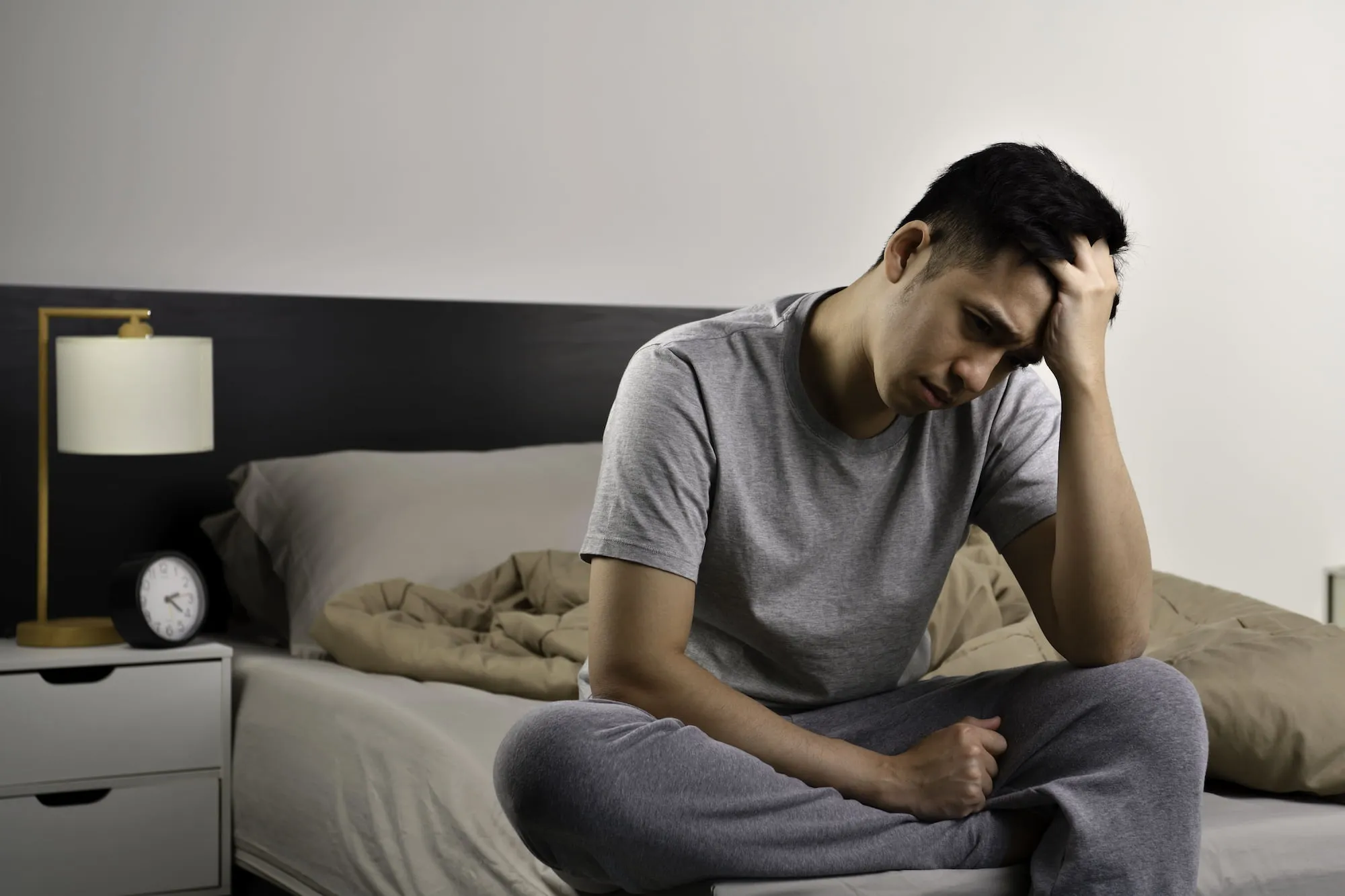 Man sitting on the edge of a bed with head in hand, appearing fatigued and downcast illustrating the importance of vitamin B12 for energy levels.