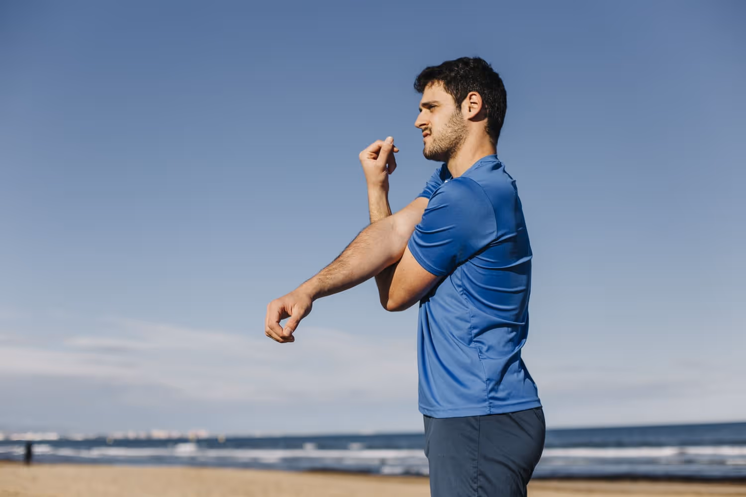 Man stretching his arm outdoors on the beach, symbolizing physical health and the role of androgen receptors in maintaining hormonal balance and fitness.