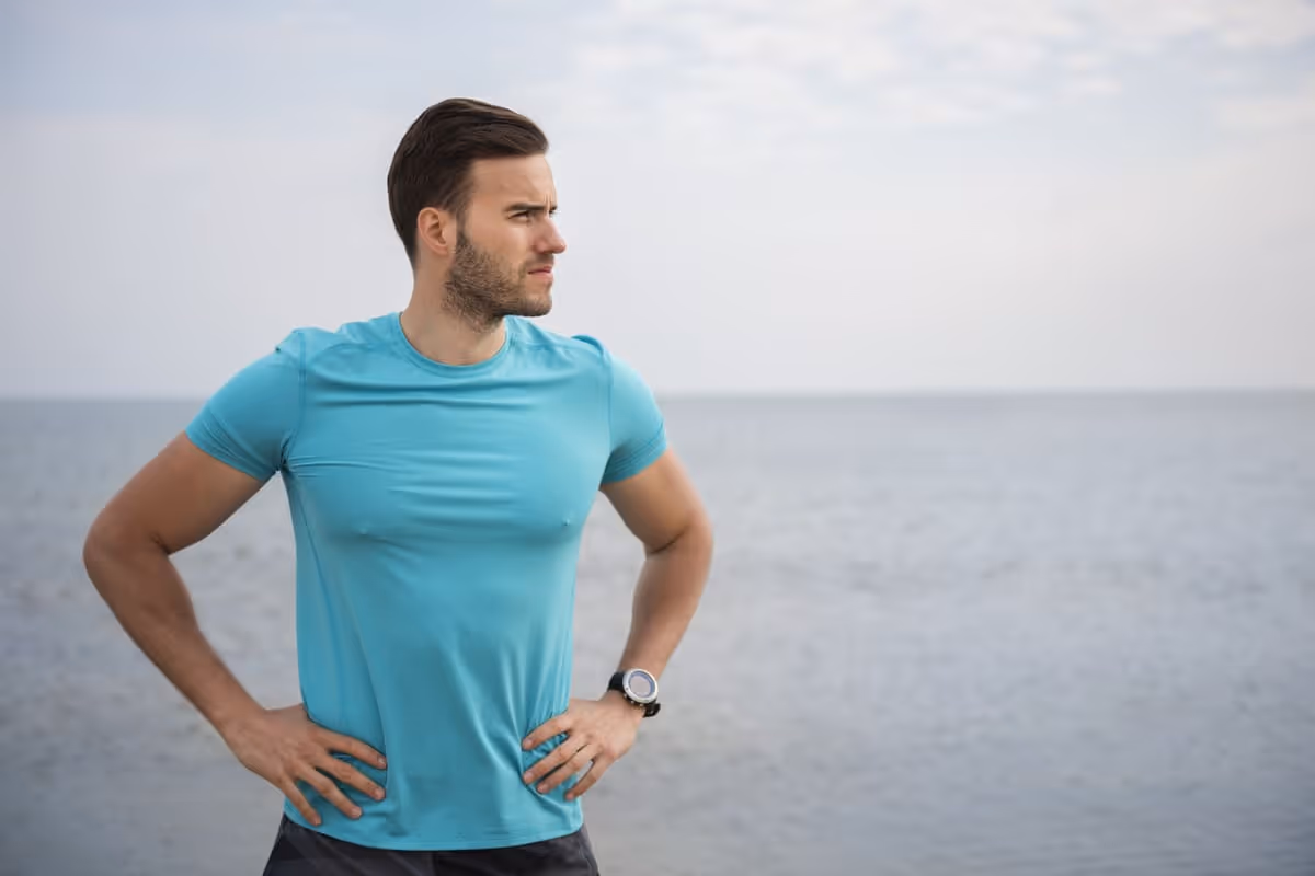 Confident, athletic man standing outdoors near the water with hands on hips, representing confidence and informed decision-making when comparing Trimix and P Shot treatment options.