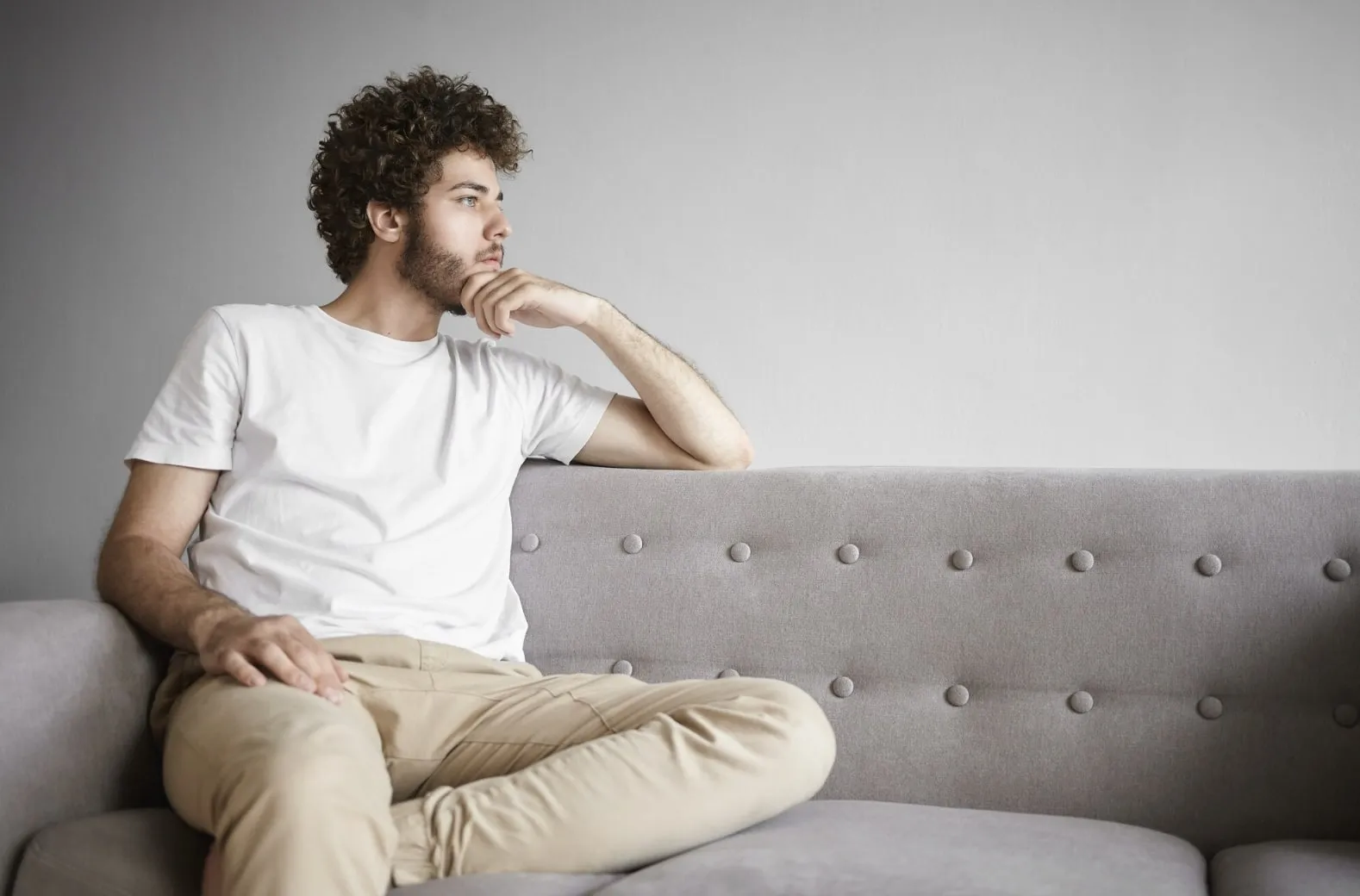 A man sitting on the couch deep in thought, representing the emotional stress and uncertainty many men feel while wondering how long erectile dysfunction recovery may take.