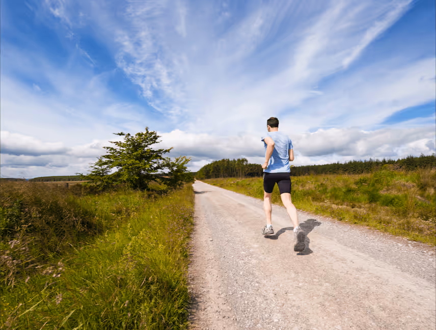 Man running along a rural gravel road surrounded by greenery, representing outdoor exercise, cardiovascular fitness, and an active lifestyle.