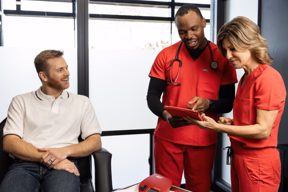A man sits with a smile while two healthcare professionals discuss treatment options on a tablet, highlighting the personalized care and attention in choosing a testosterone replacement therapy clinic.
