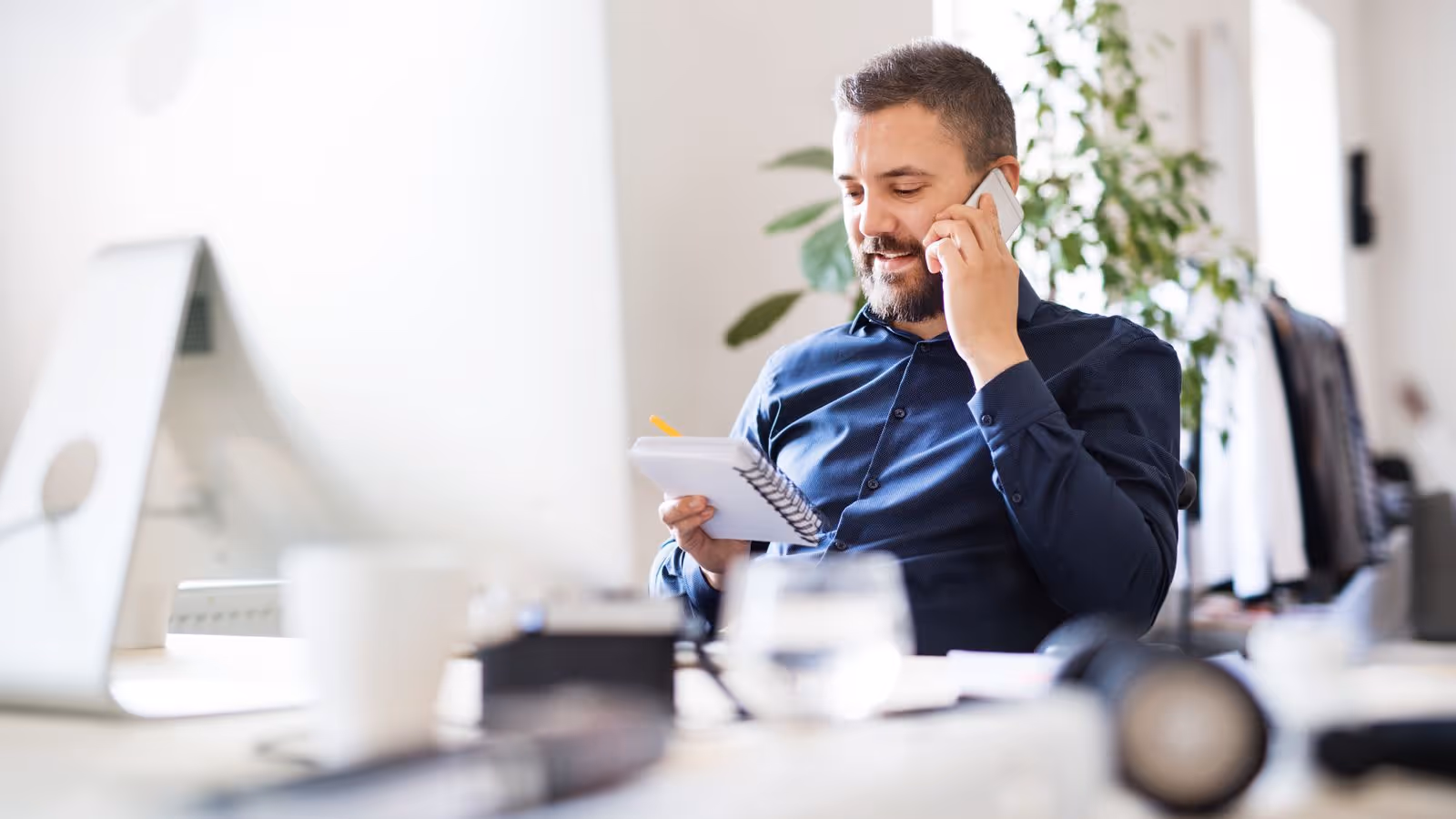 A man in an office setting takes a call while jotting down notes, reflecting the busy lifestyle of office workers who benefit from testosterone therapy.