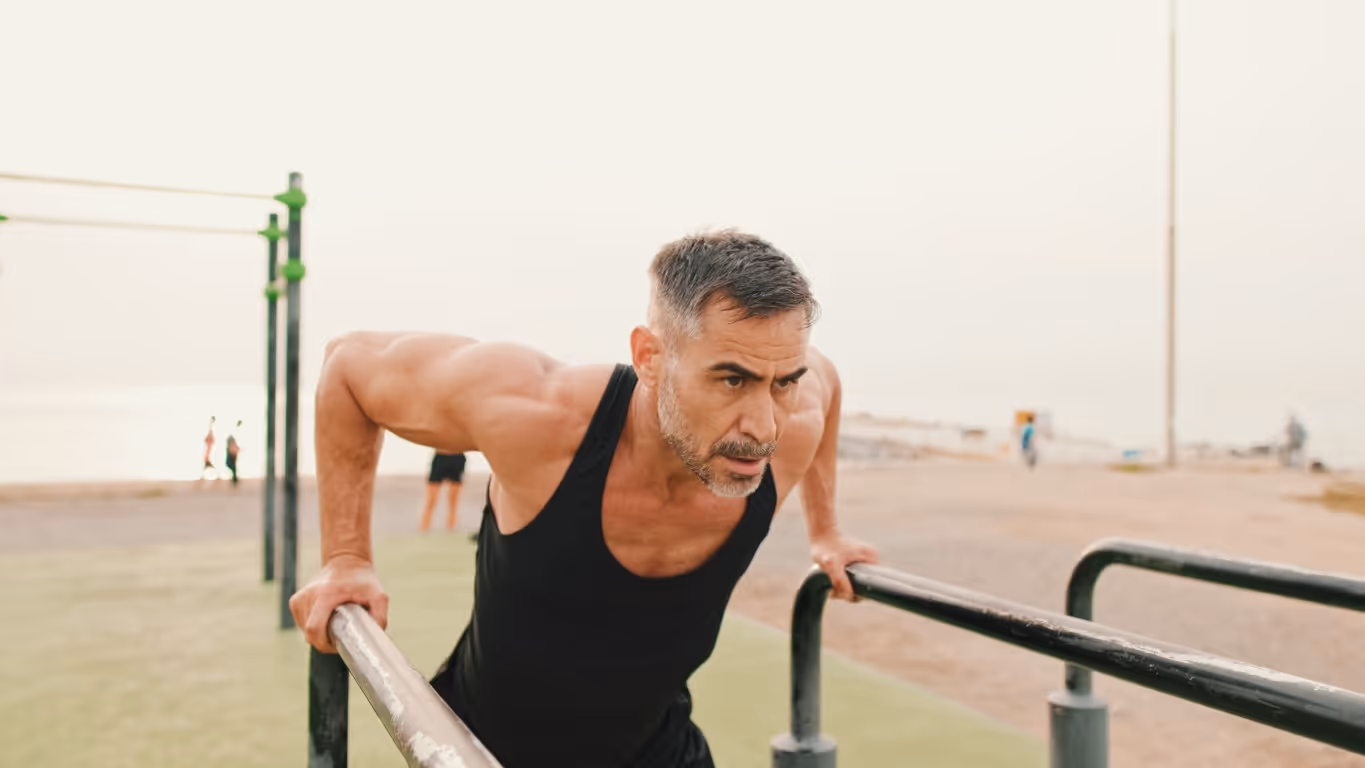 Man performing push-ups on parallel bars at an outdoor fitness area, showcasing strength and vitality that can be supported and enhanced through treatments like TRT.