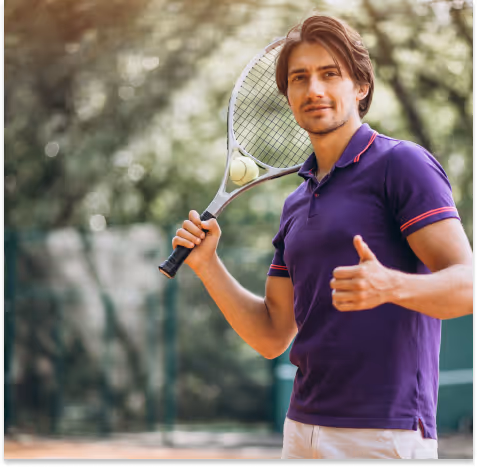 A man dressed in a purple polo shirt stands on a tennis court, holding a tennis racket with a ball in his other hand, giving a thumbs up.