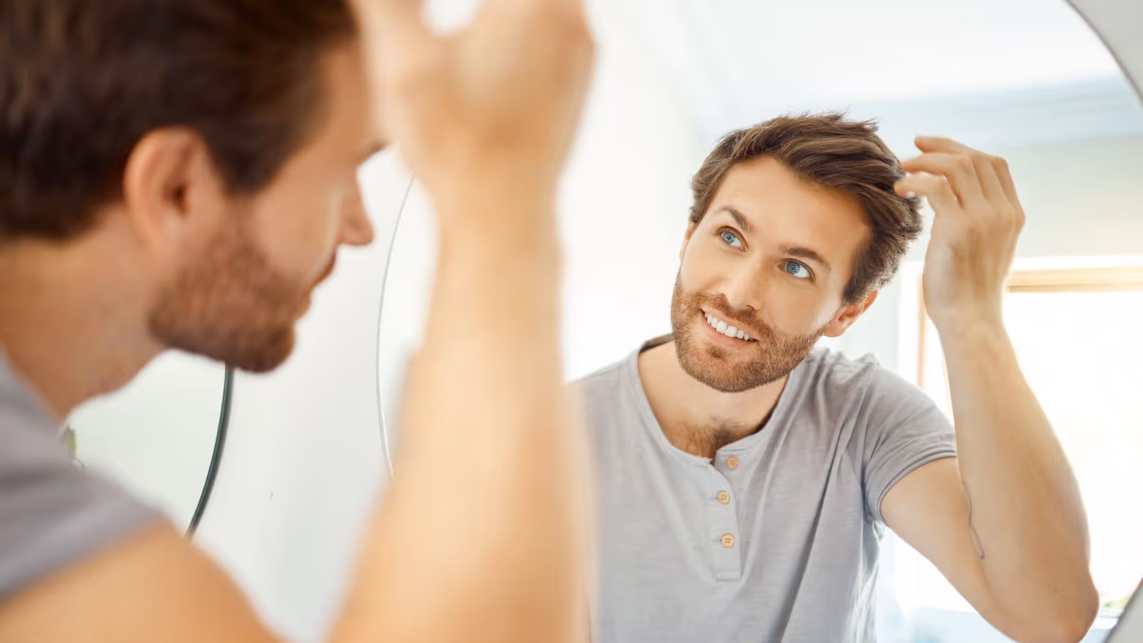 Man looking at himself in the mirror and adjusting his hair, symbolizing the positive impact of MIC and Glutathione injections on overall health and well-being for men.
