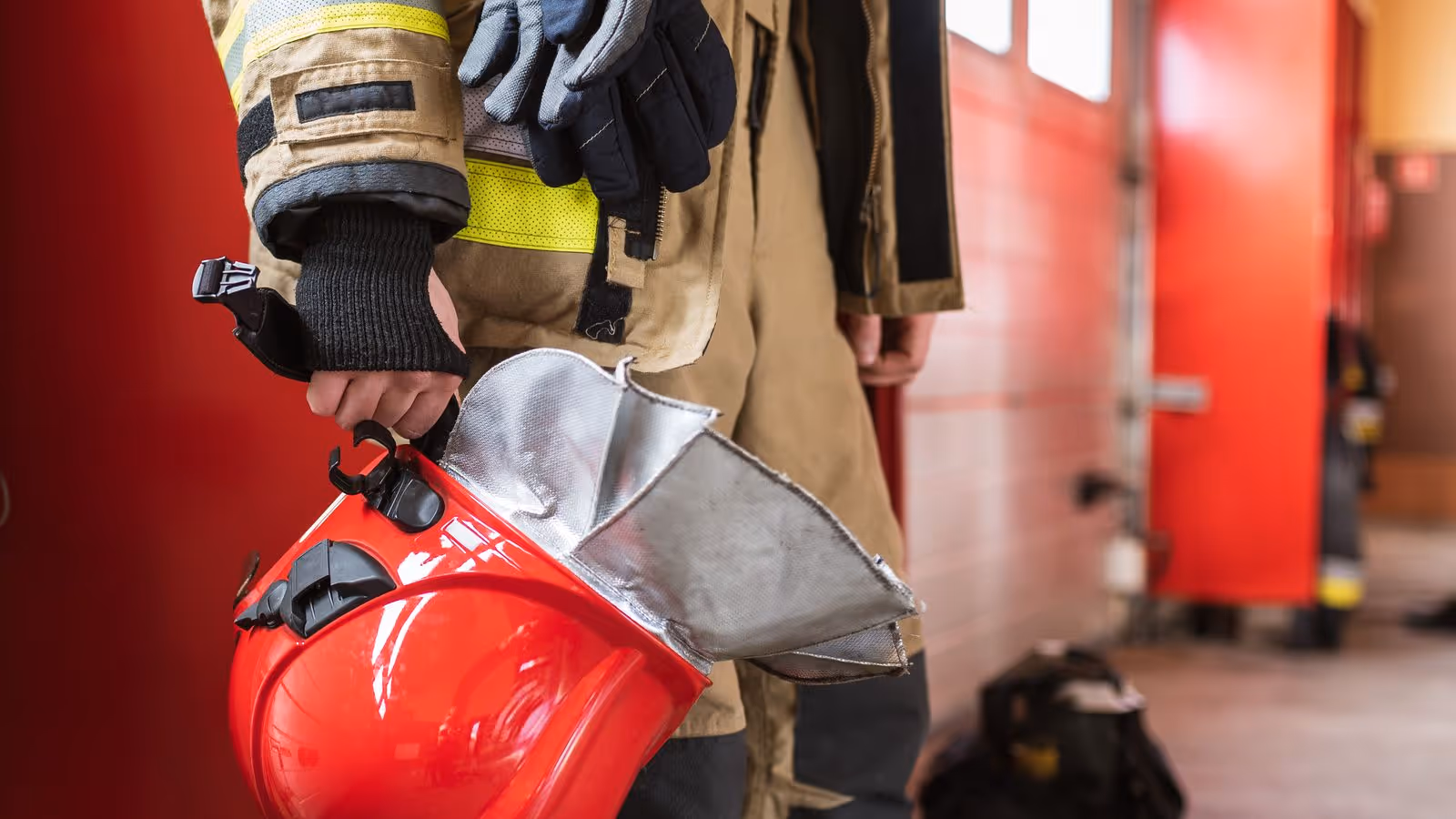 Firefighter holding helmet and gloves in fire station