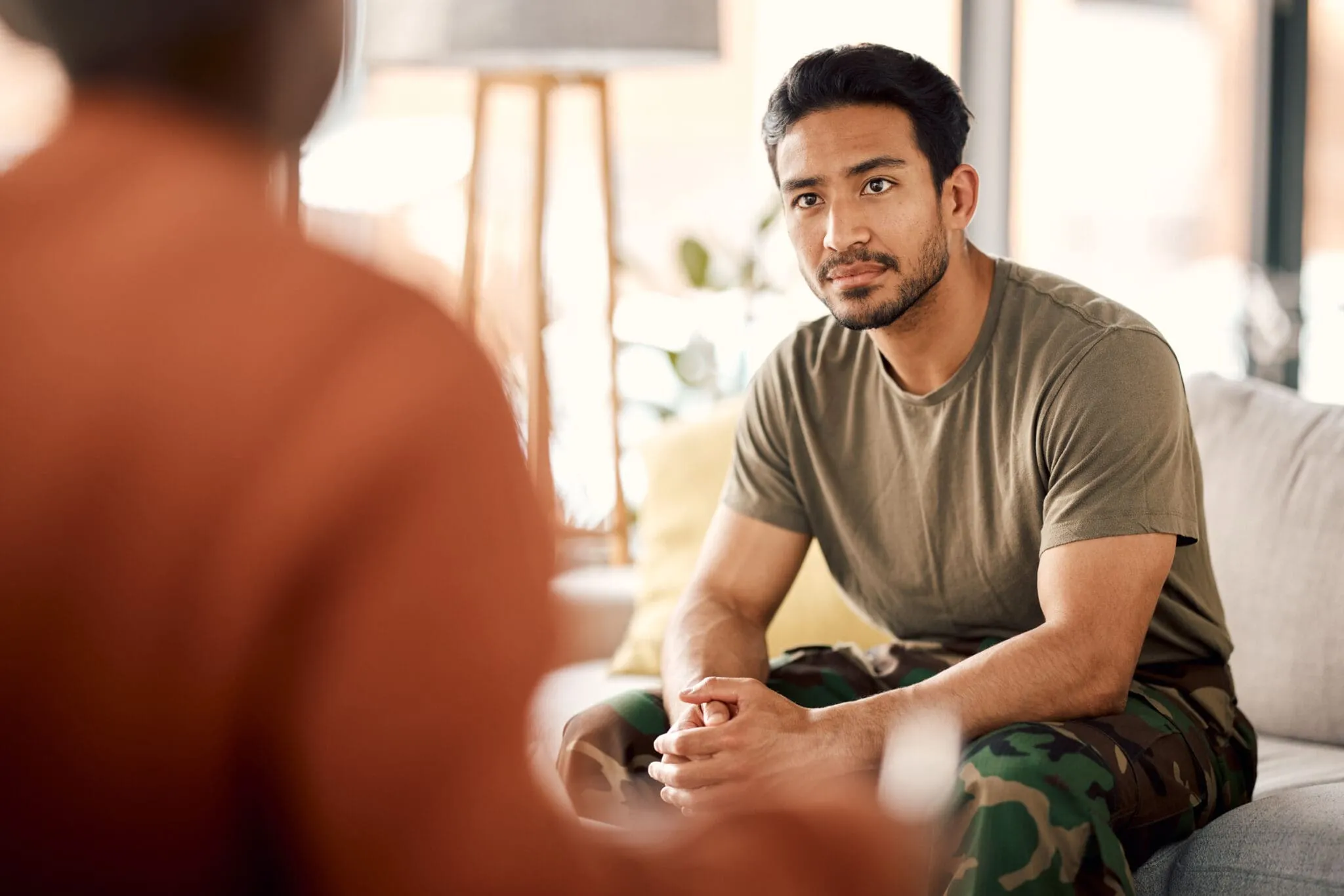 Man in green T-shirt sitting attentively on sofa in calm, softly lit room.