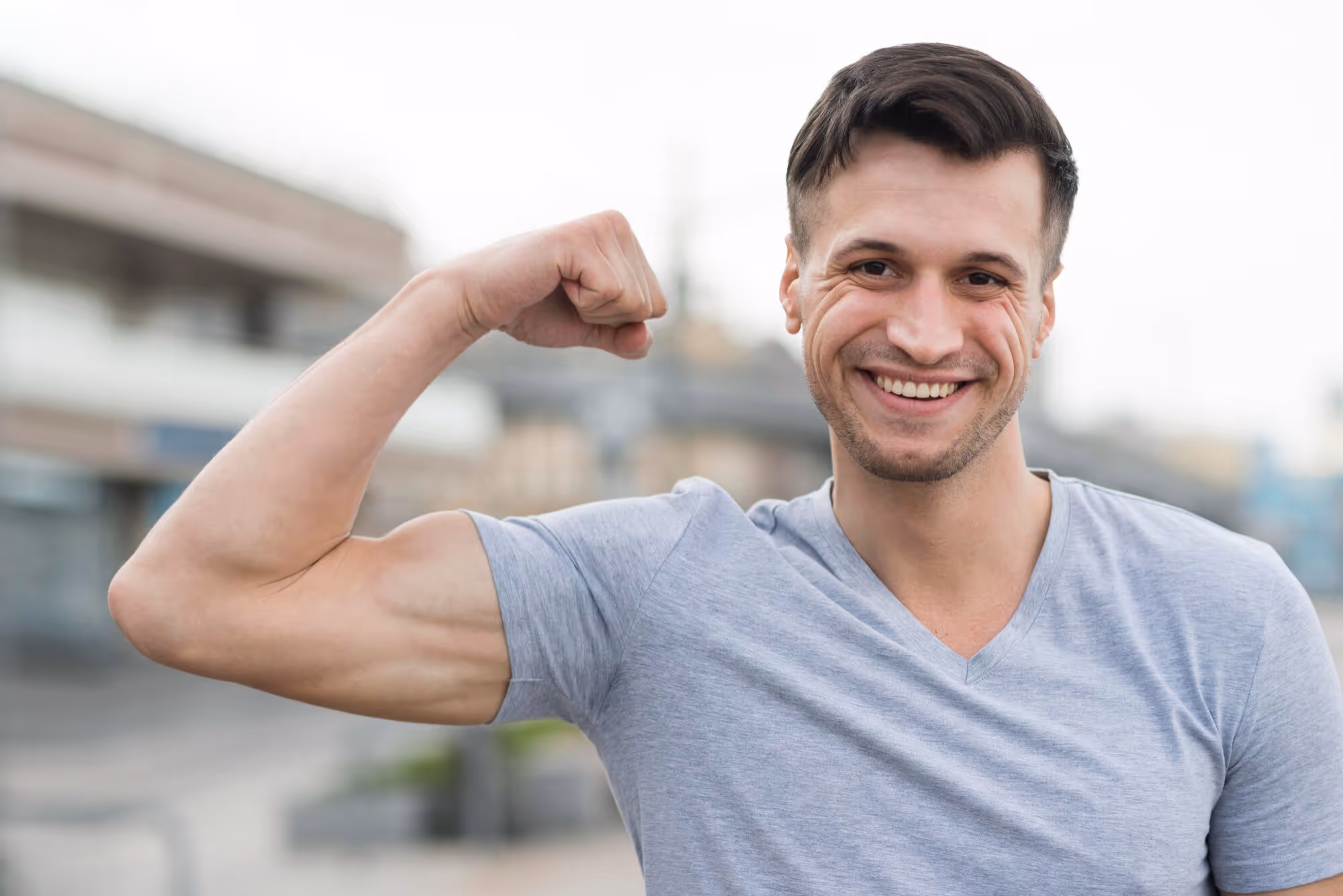 Smiling man flexing his arm outdoors, representing strength, vitality, and confidence associated with testosterone cypionate injection and testosterone optimization therapy.