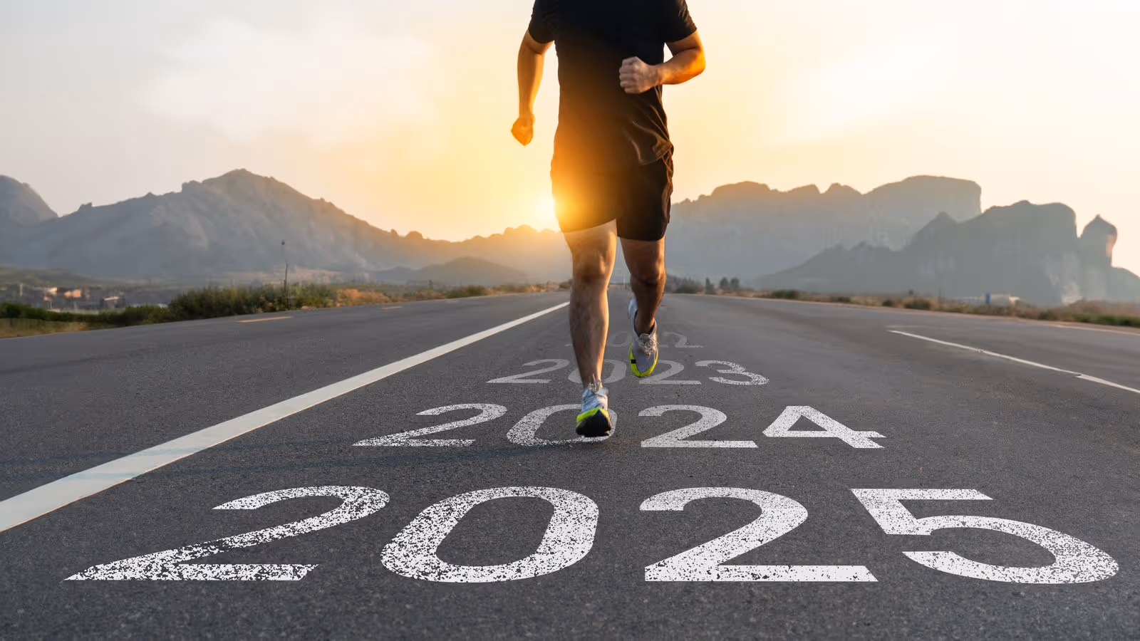 Runner on a road at sunrise with '2023', '2024', and '2025' painted on the pavement, symbolizing progress.
