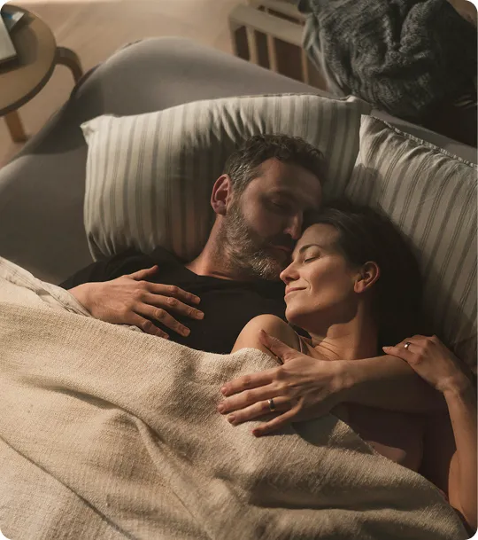 Smiling couple lying in bed together, embracing closely, representing intimacy and improved confidence from Trimix Therapy.