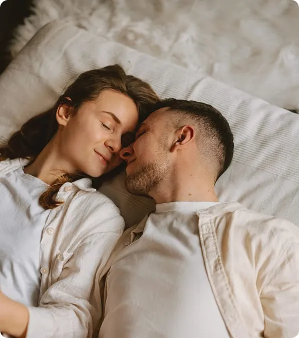 Happy couple smiling and relaxing on the bed, symbolizing intimacy, confidence, and improved sexual performance after effective treatment with Viagra or Cialis.