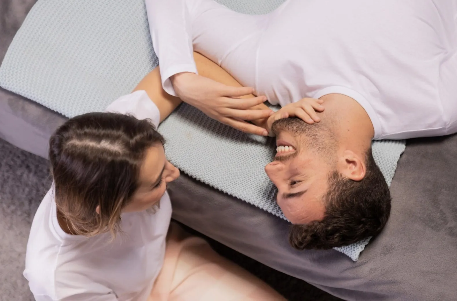 Man and woman smiling while lying on a bed, representing improved intimacy through natural ED treatments.