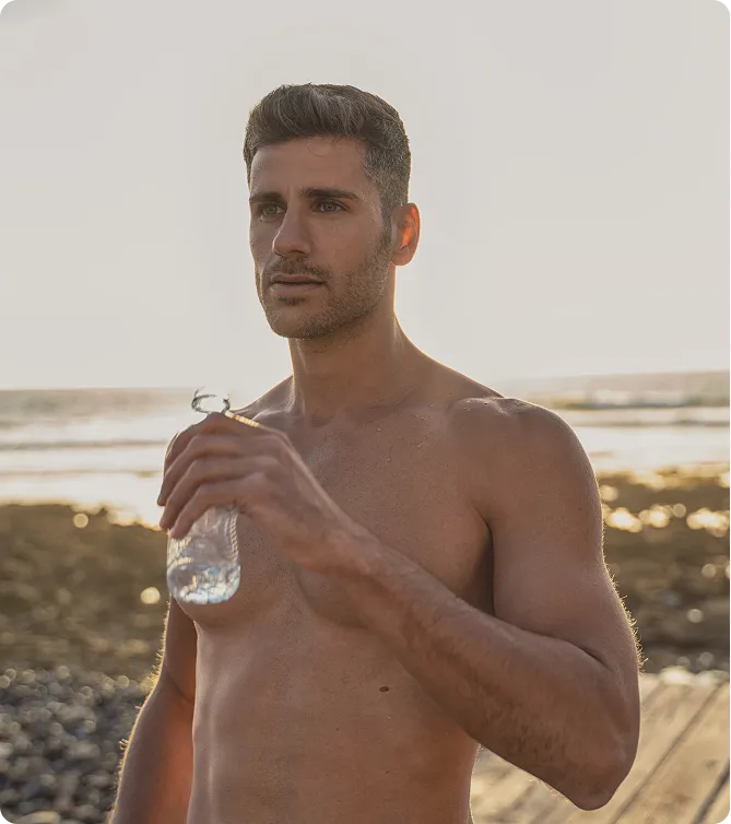 Fit man drinking water after a workout on the beach, representing weight-loss and metabolic benefits of Tirzepatide therapy.