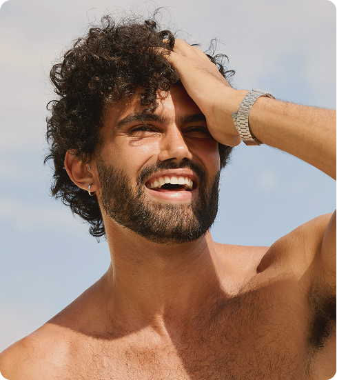 Man with thick curly hair smiling outdoors, representing scalp health and hair density benefits of Minoxidil treatment.