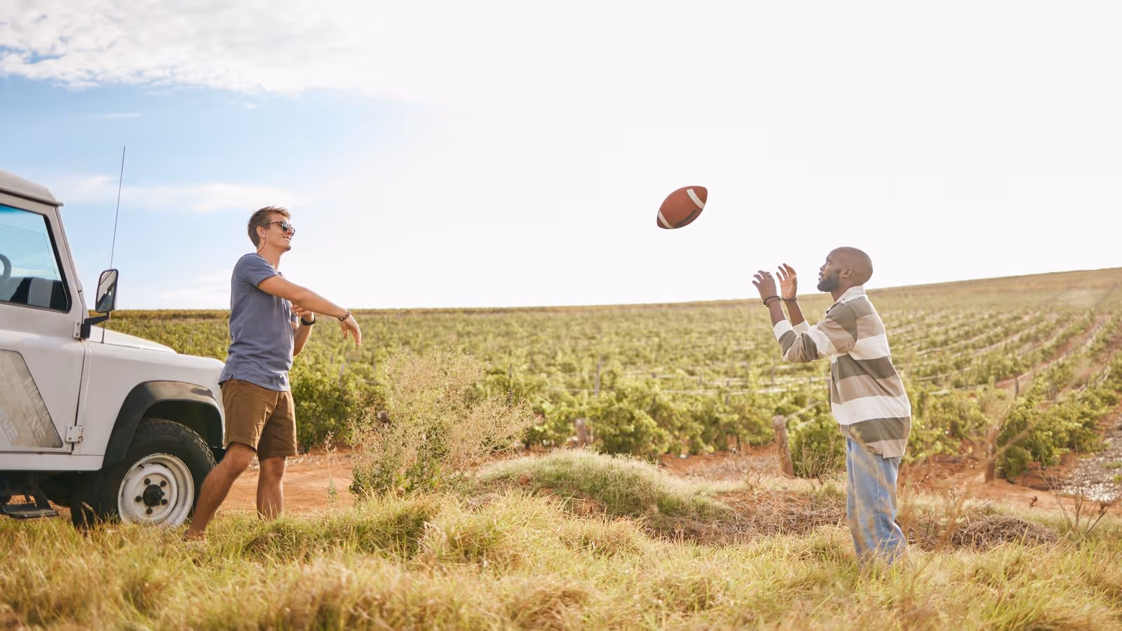 Two people play catch with a football in a sunny vineyard, creating a relaxed vibe.