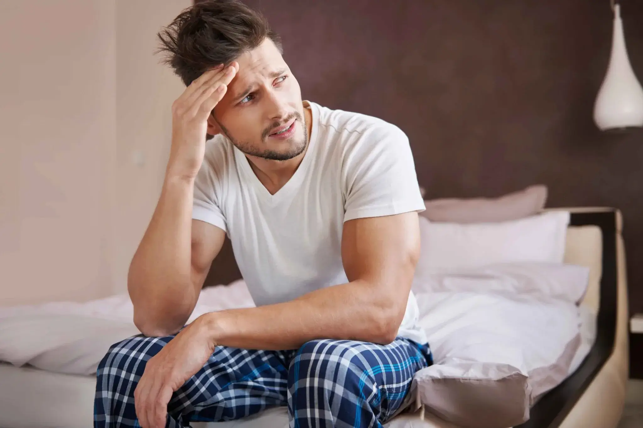 Concerned man sitting on bed in pajamas, illustrating potential health issues linked to low testosterone.