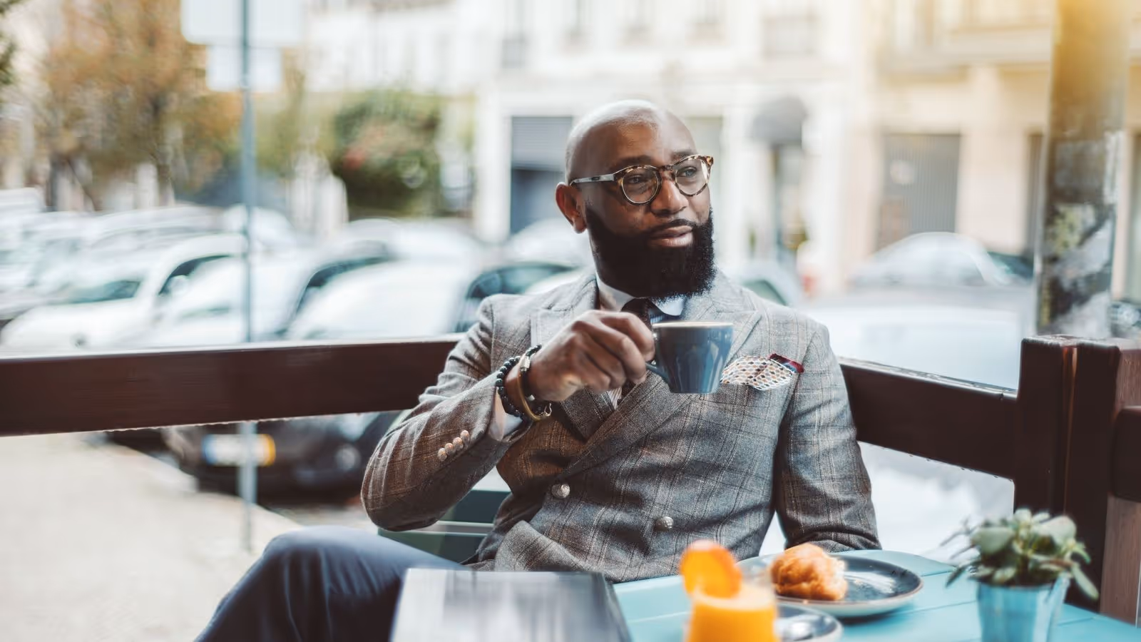 Man in suit drinks coffee at outdoor café with breakfast.
