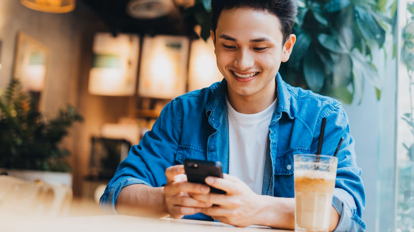 Smiling person checks phone at café with iced coffee — relaxed moment linked to enclomiphene lifestyle.