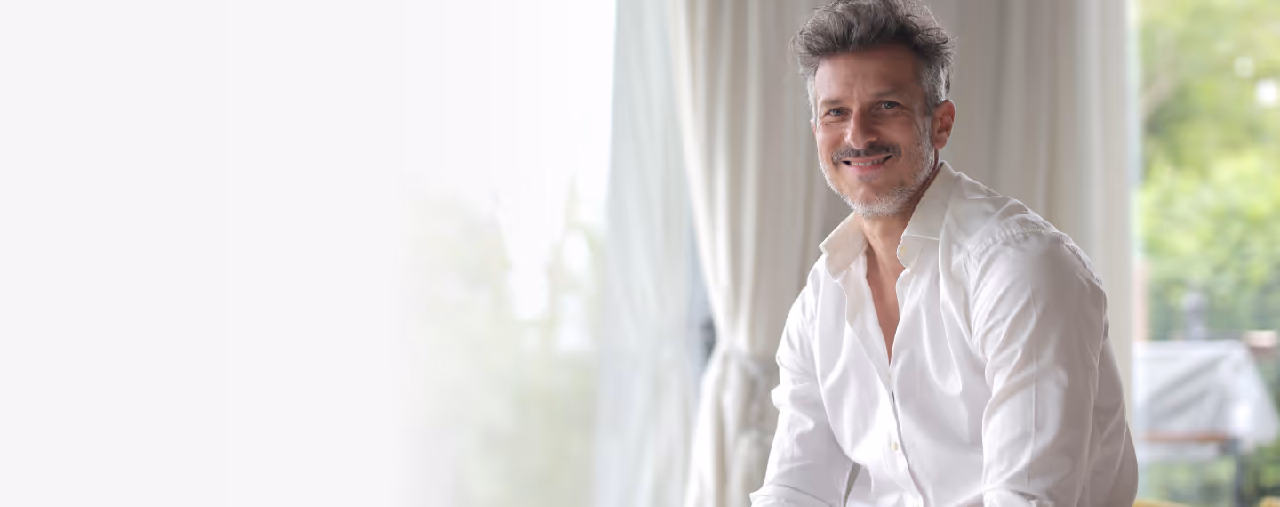 Smiling man in white shirt sitting in bright, relaxed room.