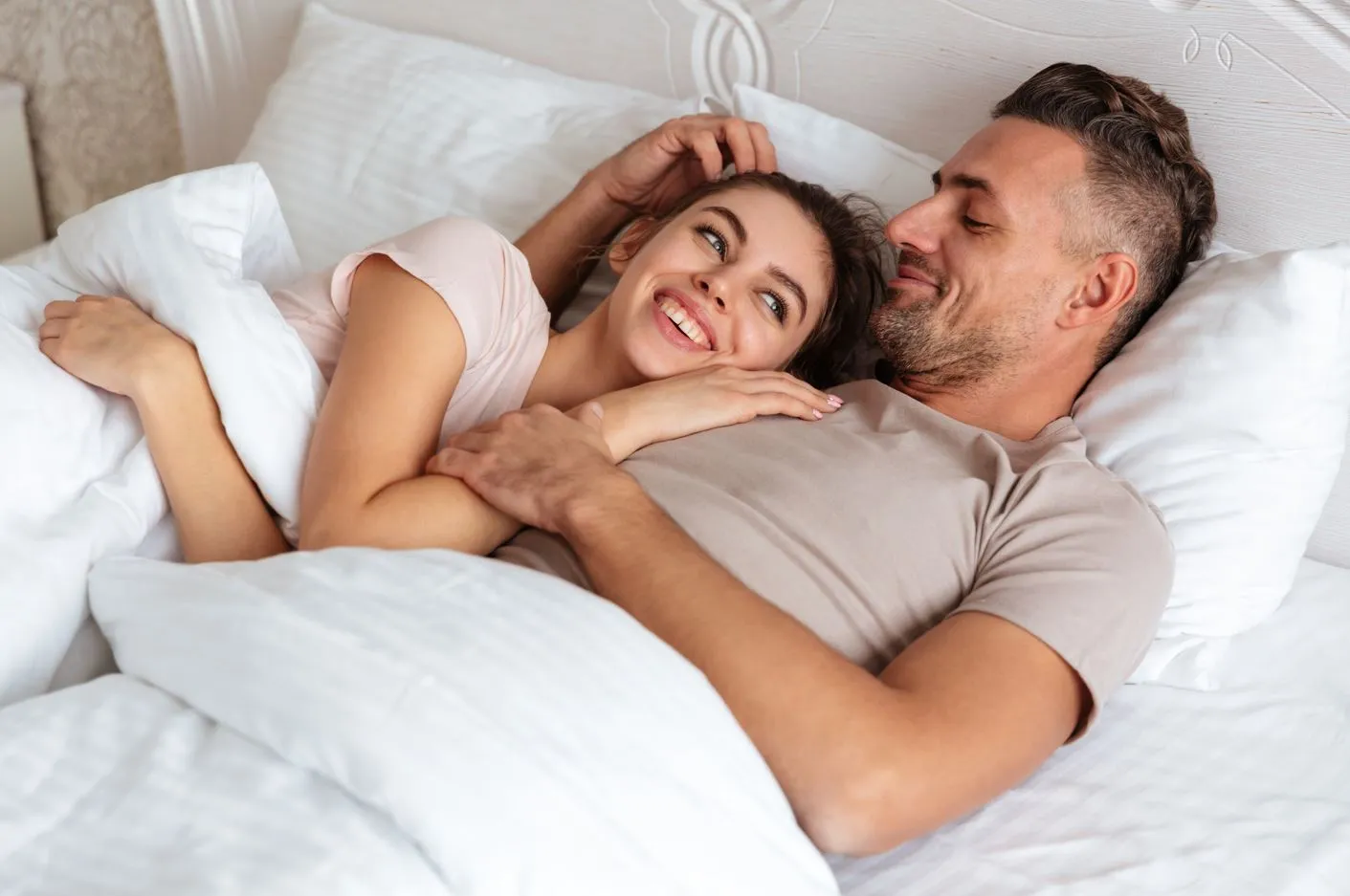 Smiling couple cuddling in bed, symbolizing improved intimacy and sexual performance after PRP treatment for erectile dysfunction.