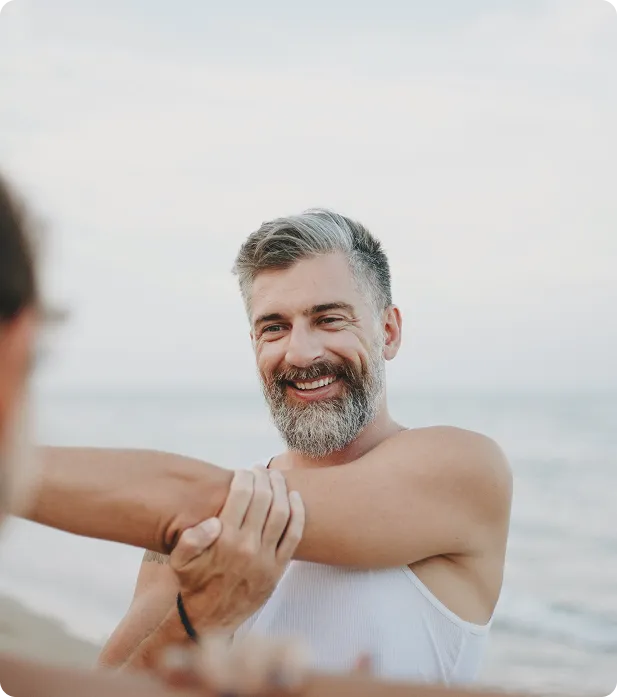 Middle-aged man stretching on the beach, representing improved energy, recovery, and vitality supported by GHRH peptide therapy.