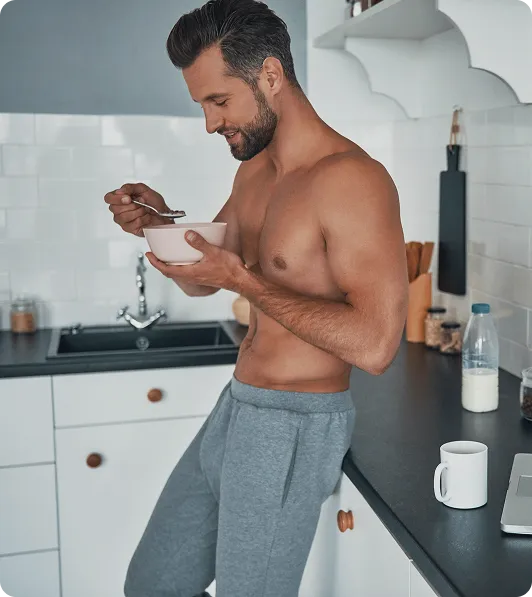 Man eating a bowl of cereal shirtless in a modern kitchen, representing daily lifestyle routines during enclomiphene hormone therapy