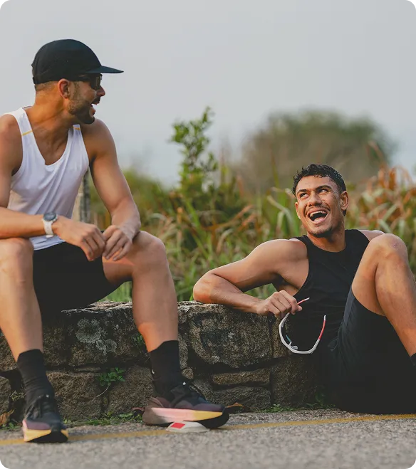 Two men resting outdoors after a workout, sitting on a stone ledge and talking, representing fitness progress and body composition scans at Gameday Men’s Health.