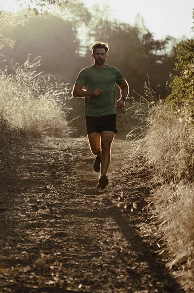 Fit man running along a scenic path during sunrise, representing the energy, vitality, and improved well-being that can result from Clomid or Enclomiphene therapy.