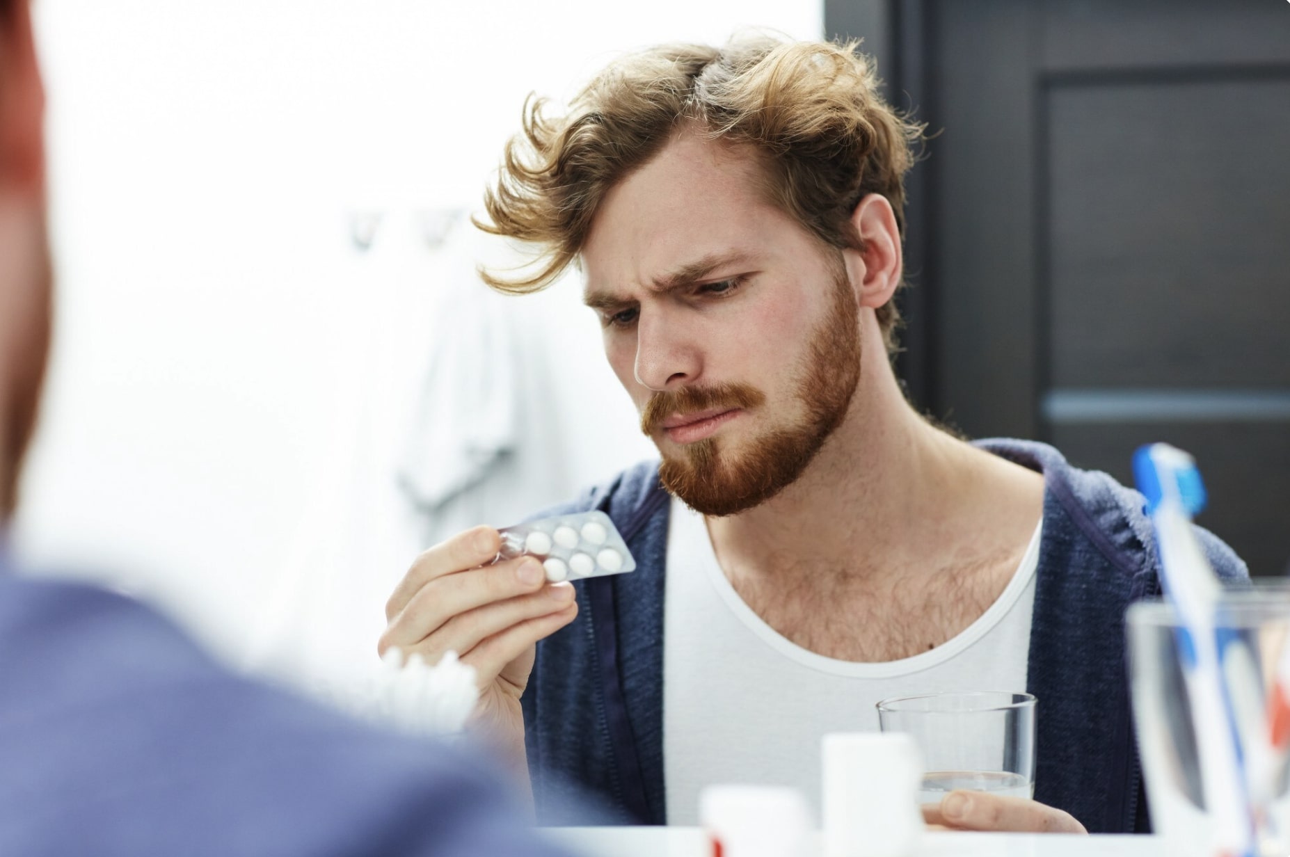 Thoughtful man holding pills as he compares oral testosterone and injectable TRT treatments.