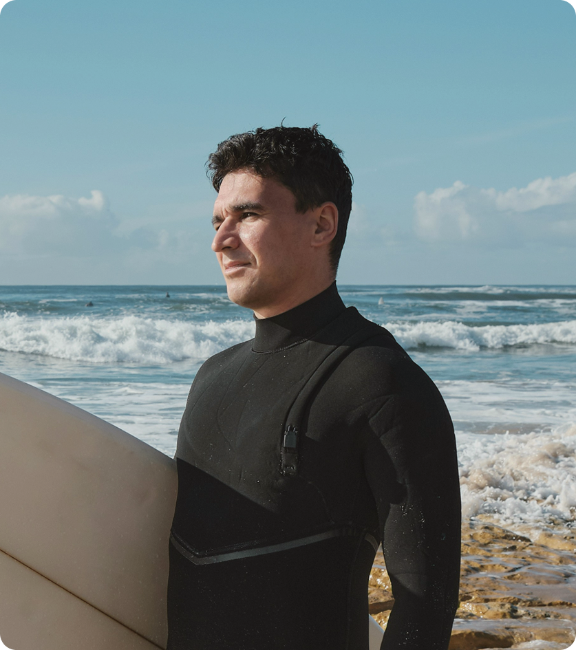 Man standing on the beach near the ocean after surfing, reflecting confidence and active living associated with PRP for Hair Loss in Markham, ON.