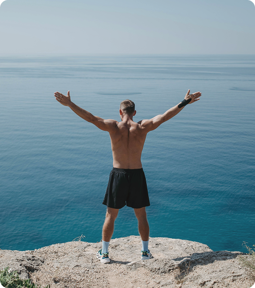 Fit man standing on a rock overlooking the ocean, conveying resilience and perspective aligned with wellness care through Vitamin C Injections in Burlington, ON.